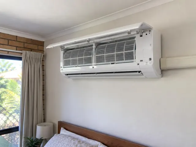 Split system on a bedroom wall with open front panel and visible filters above a bed in Bundall