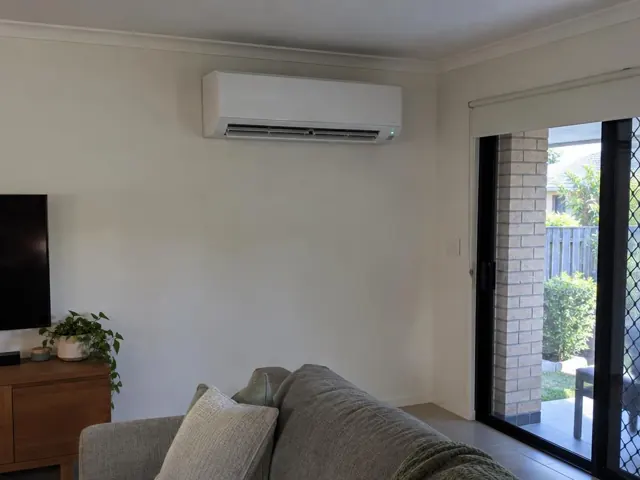 Wall-mounted split system above a living room wall beside a sliding glass door in Southport